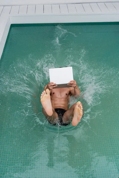 Top view of man with computer falling in pool with turquoise water - foto de stock