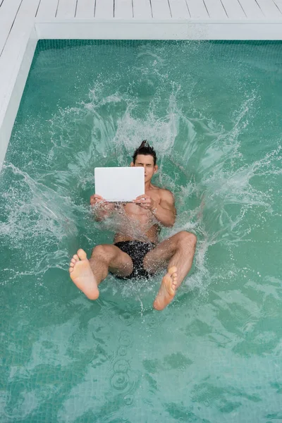 Top view of freelancer jumping with laptop in pool with turquoise water — Stock Photo