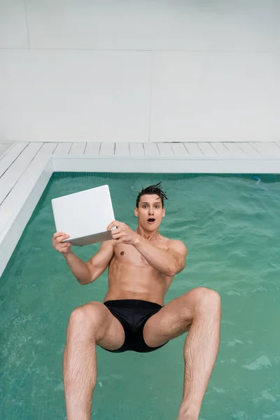 Astonished man falling in pool with laptop while looking at camera — Stock Photo