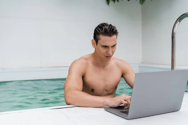 Sportive man with wet hair using laptop near pool — стоковое фото