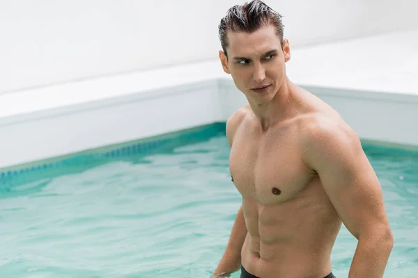 Wet sportive man looking away near pool with turquoise water — Stockfoto