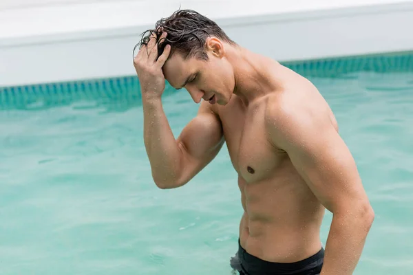 Athletic man with wet hair standing in pool with turquoise water - foto de stock