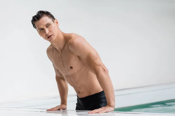 Wet man with sportive body looking away at poolside — Stock Photo