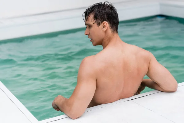 Rückansicht eines Mannes mit nassen Haaren, der im Pool mit türkisfarbenem Wasser steht — Stockfoto