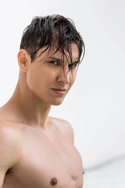 Wet sportive man with perfect skin looking at camera on white background — стоковое фото