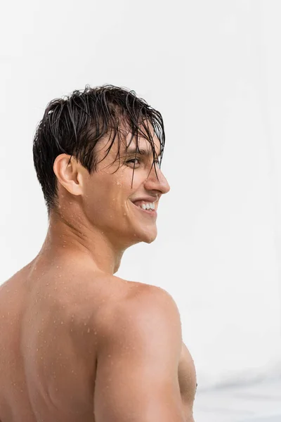 Wet and happy man with bare shoulders looking away on white background — стоковое фото