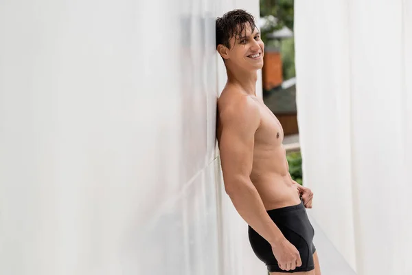 Cheerful shirtless man with athletic torso looking at camera near white wall — Stock Photo