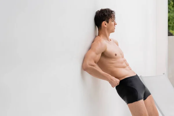 Wet man in swimming trunks leaning on white wall outdoors - foto de stock