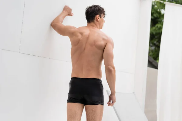 Back view of shirtless man with athletic body standing by white wall — Stock Photo