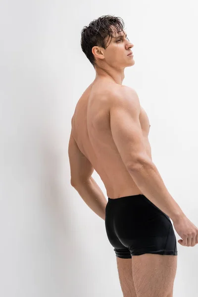 Wet athletic man in swimming trunks looking away on white background — Photo de stock