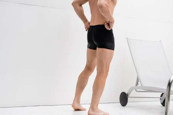 Partial view of barefoot shirtless man adjusting swimming trunks outdoors — Stock Photo