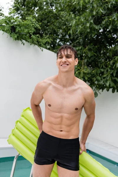 Веселий чоловік у басейні стоїть з плаваючим матрацом на відкритому повітрі — стокове фото