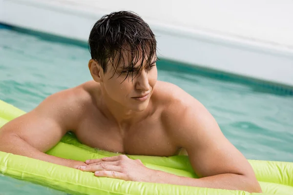 Мокрий чоловік плаває в басейні з надувним матрацом і дивиться в сторону — стокове фото