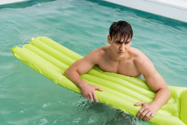Мокрий чоловік плаває з надувним матрацом у басейні з бірюзовою водою — стокове фото