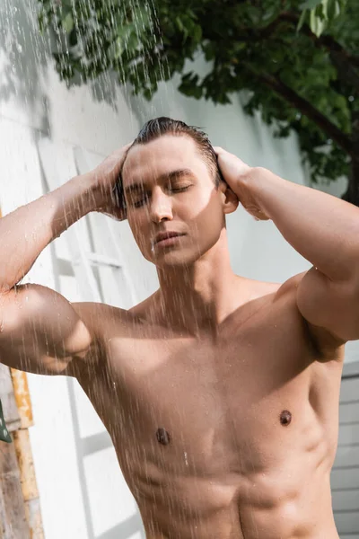 Muscular man with closed eyes taking shower outdoors — Stockfoto