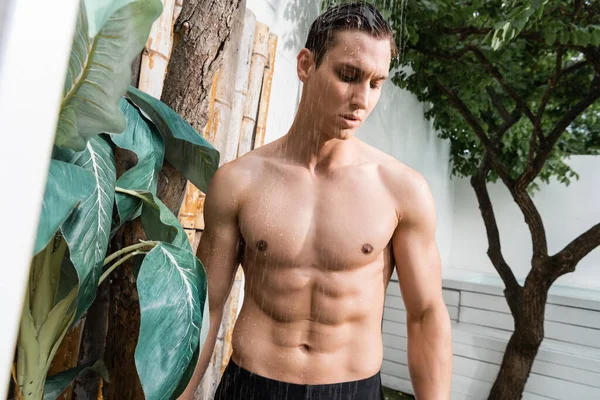 Man with athletic torso standing under shower outdoors - foto de stock