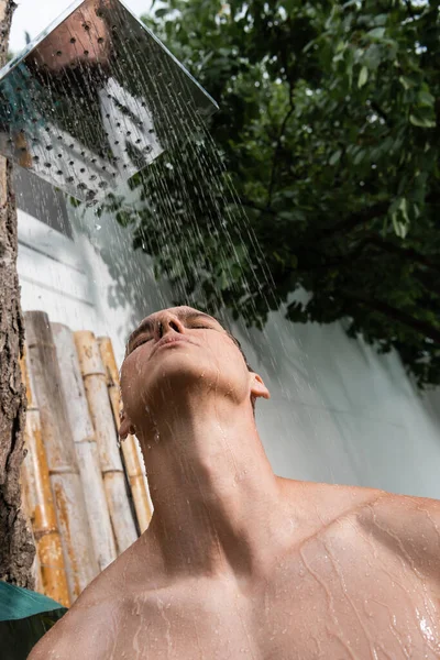 Low angle view of man with closed eyes taking shower outdoors - foto de stock