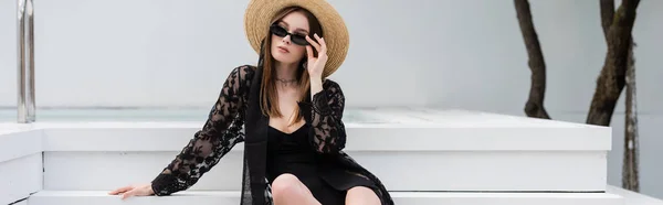 Stylish woman in swimsuit and sun hat holding sunglasses near pool, banner — Stock Photo