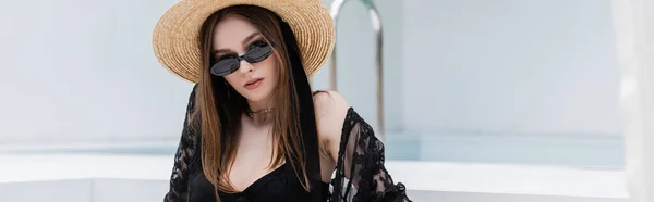 Fashionable woman in swimsuit and straw hat looking at camera at resort, banner — стоковое фото