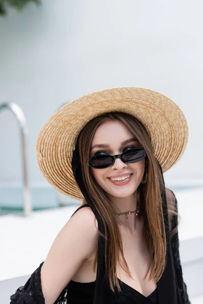 Smiling and stylish woman in swimsuit and sunglasses looking away at resort — Foto stock