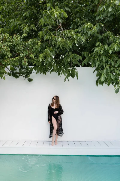 Stylish woman in swimsuit standing near wall and swimming pool — Photo de stock