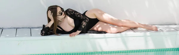 Pretty young woman in black swimsuit lying near swimming pool at resort, banner — Stock Photo