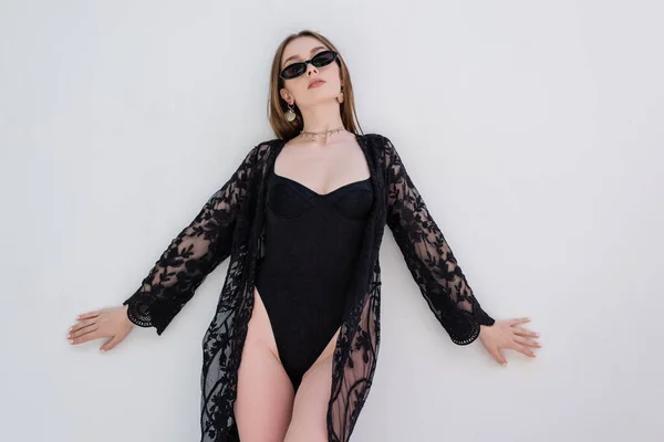 Trendy woman in black robe and swimsuit posing near wall at resort — Foto stock