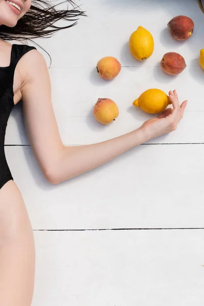 Cropped view of cheerful woman in swimsuit lying near fresh fruits on floor at resort — Foto stock