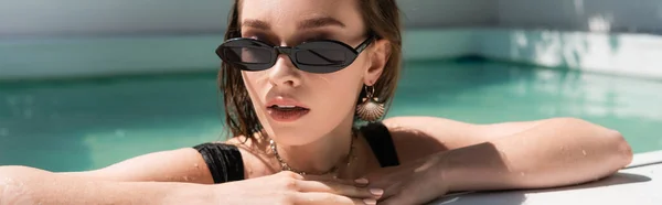 Portrait of young and stylish woman in black sunglasses resting in swimming pool, banner — Photo de stock