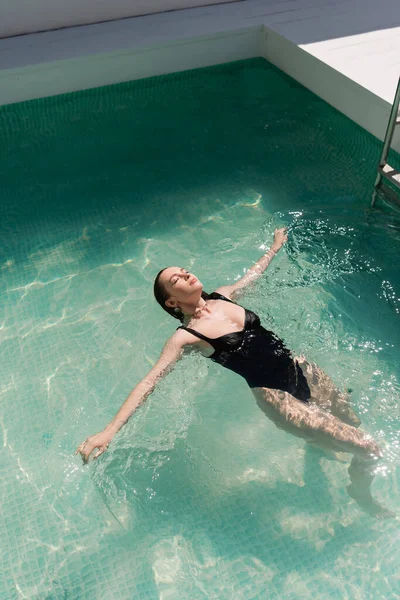 Top view of young woman in stylish black swimsuit swimming in pool — Stock Photo