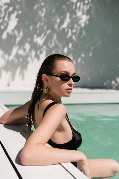 Pretty young woman with wet hair and trendy sunglasses sunbathing in swimming pool — Foto stock