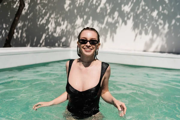 Happy young woman with wet hair and stylish sunglasses sunbathing while swimming in pool — Foto stock