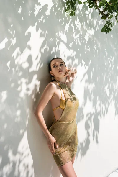 Pretty woman in summer dress standing near while wall with shadows — Fotografia de Stock