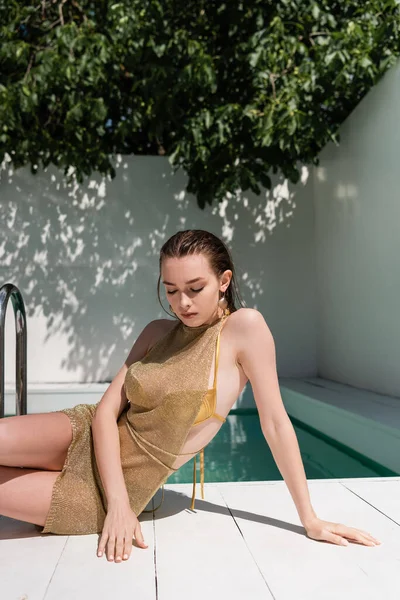Stylish woman in summer dress and swimwear sitting near pool on luxury resort - foto de stock