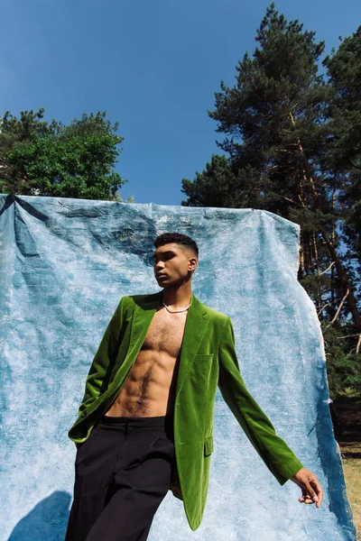 Young african american man in green blazer posing near blue drape in park - foto de stock