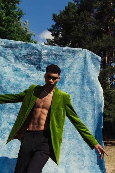 African american man in green blazer posing with outstretched hands near blue cloth in park — Photo de stock