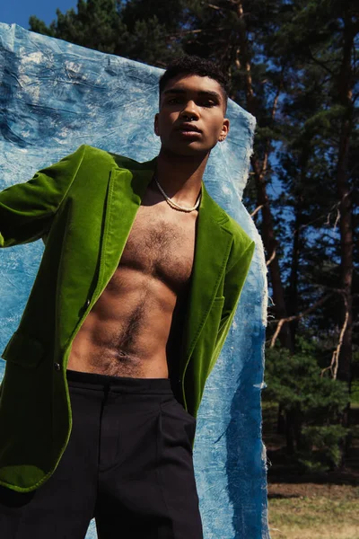 Low angle view of african american man in green blazer and beads near blue cloth in park — Fotografia de Stock