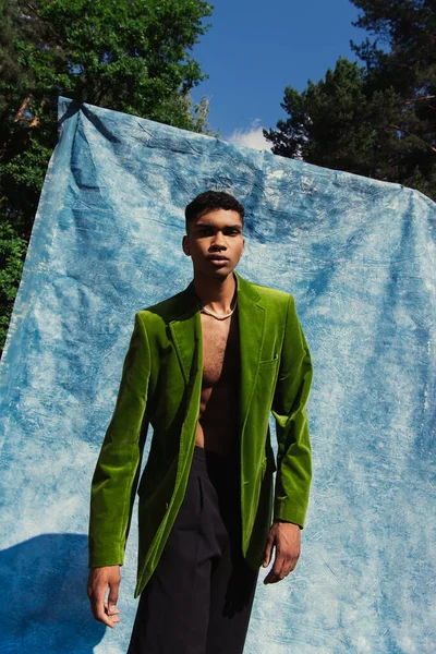 African american man in green blazer and black shorts near blue drape in park - foto de stock