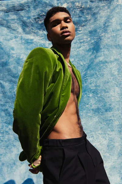 Low angle view of african american man in green blazer looking at camera near blue drape outdoors — Stock Photo