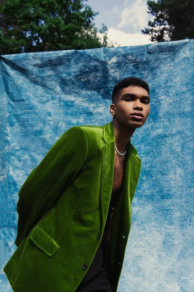 African american man in green velvet blazer looking at camera near blue cloth outdoors — стоковое фото