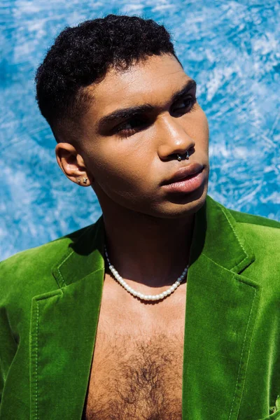 Portrait of stylish african american man in piercing looking away near blue drape on background — Fotografia de Stock