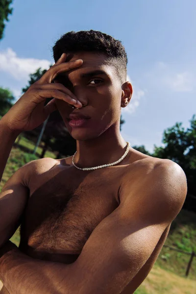 Young shirtless african american man obscuring face with hand while looking at camera outdoors — Fotografia de Stock