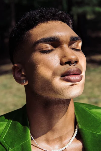 Portrait of african american man with closed eyes and piercing in sunshine outdoors — Stock Photo