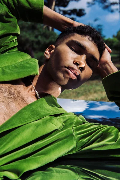 Trendy african american man with piercing and hands on head posing on reflective surface in park — Photo de stock