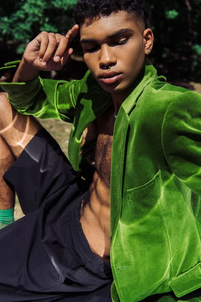 Модний афроамериканський чоловік у зеленому блістері та чорних шортах, що сидить на відкритому повітрі — стокове фото