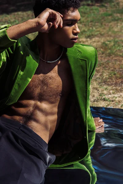 African american man in green velvet blazer sitting on flexible mirror with hand near head — Foto stock