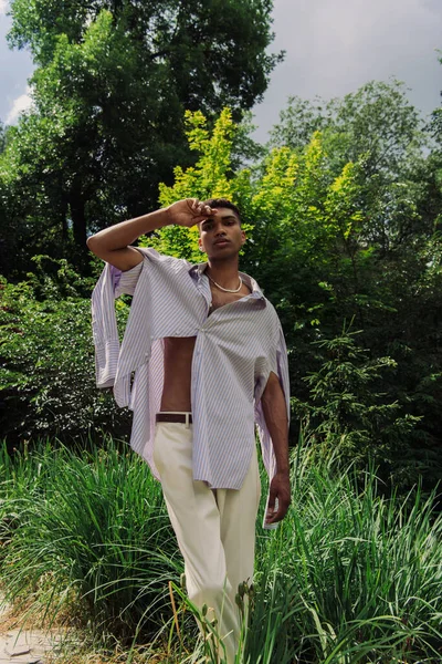 African american man in fashionable shirt holding hand near head and looking at camera in park — Photo de stock