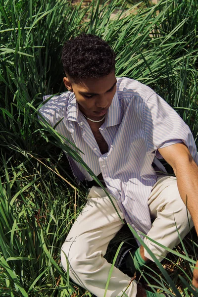 High angle view of african american man in blue shirt sitting on grass in park — Foto stock