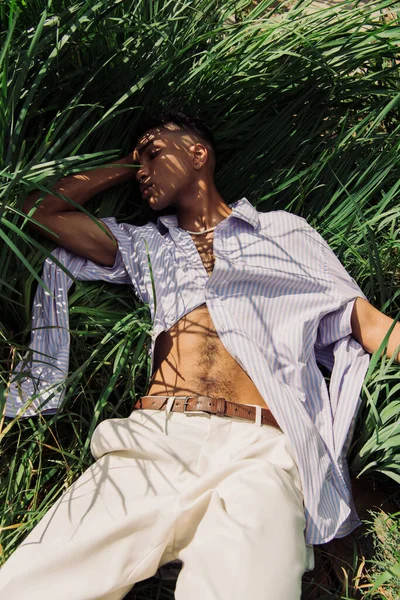 Високий кут зору афроамериканця в модному одязі, що спить на траві в парку — стокове фото