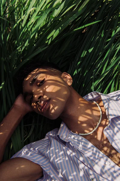 Вид зверху на афроамериканця в бісері, що лежить на зеленій траві і дивиться на камеру — стокове фото